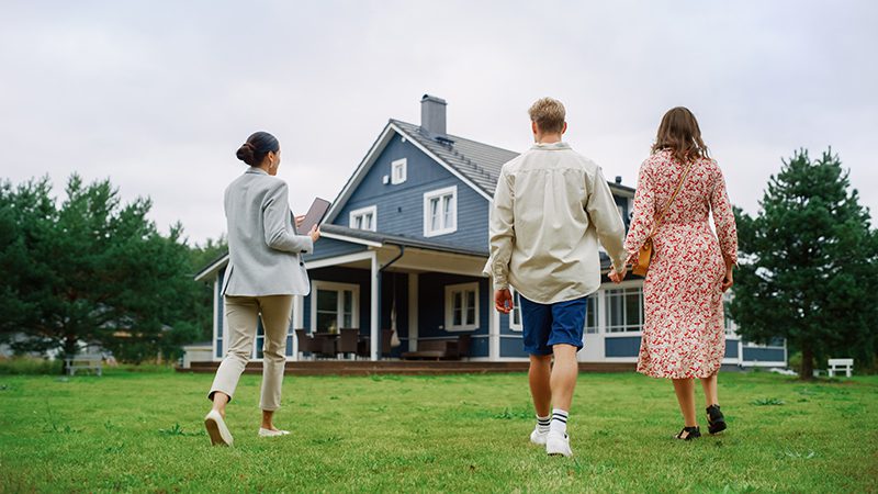shutterstock_2222205131 A couple and a real estate agent walking towards a house